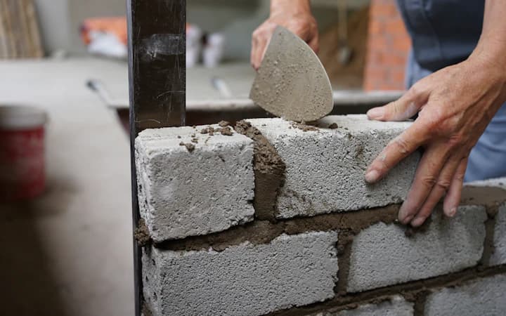 Des mains montent un mur de parpaings à la truelle