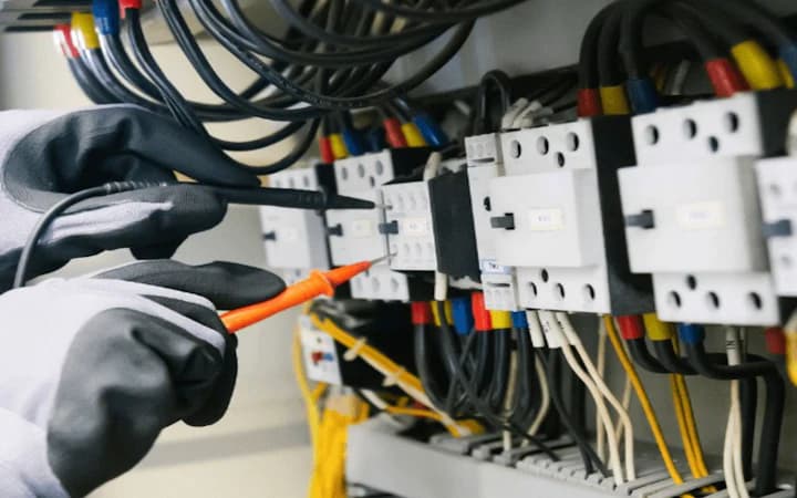 Des mains gantées testent un tableau électrique