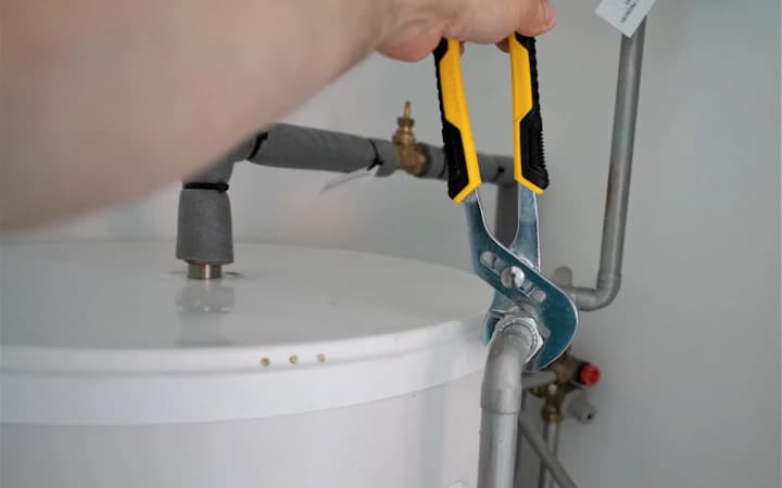 Une main serre à la pince le raccord d’un chauffe-eau